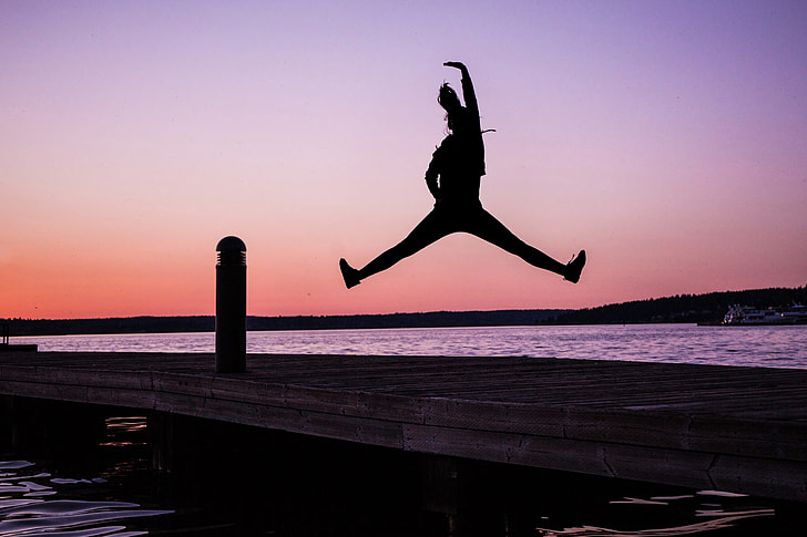 Silhouette of woman jumping on the coast at sunset