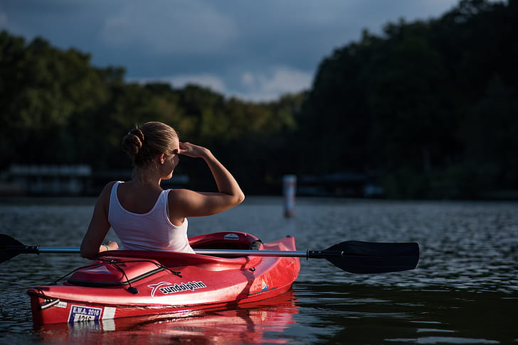 woman riding kayak holding paddle in the middle of calm body of water surrounded by trees