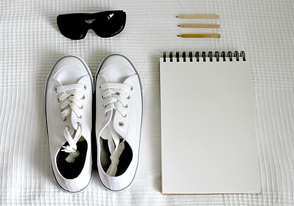 pair of white low-top sneakers near the white notebook