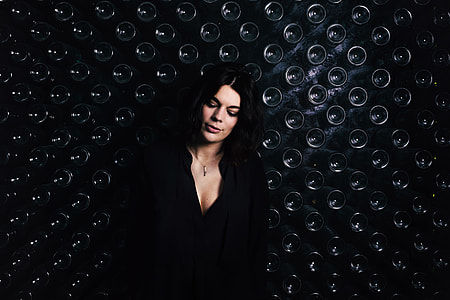 Image of a woman standing by a wall containing glass bottles