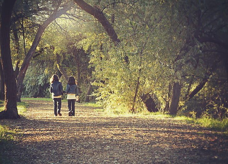 two girl wearing blue denim jackets walking on the forest