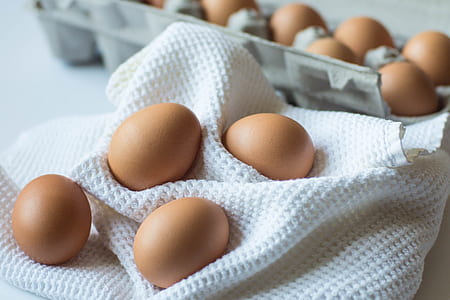 photo of brown eggs with trays near white textile