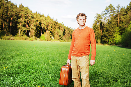 man wearing orange Henley long-sleeved shirt with brown denim bottoms on green grass field during daytime