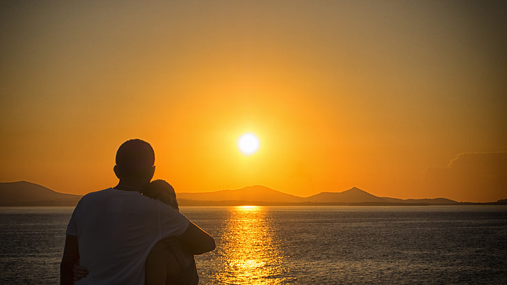 couple hugging near calm sea during golden hour