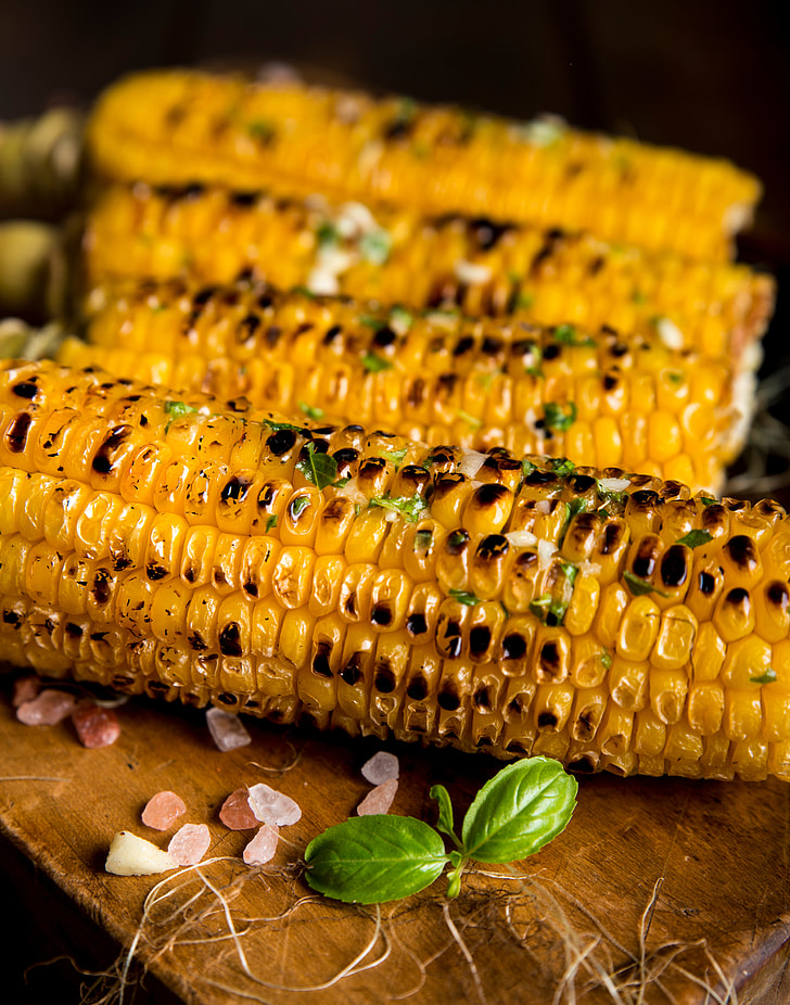 four grilled corn on top of brown wooden table