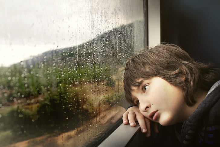 boy resting cheek on hand while looking outside window