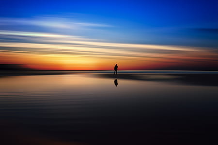 silhouette of man near body of water during sunset