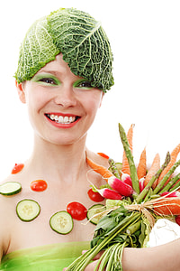 woman with lettuce on her head and sliced tomato and cucumber surrounded on her leg with carrots and spinach on her right hand