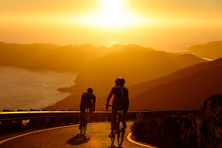 Two men on cycling exercises on bicycles on the coast at sunset
