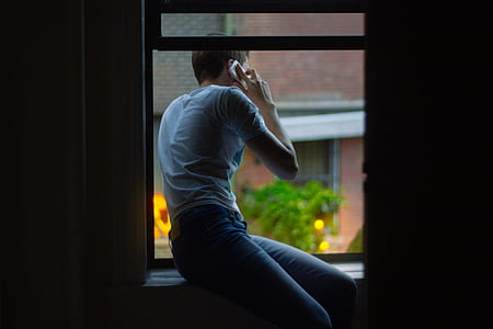 man sitting on window using smartphone