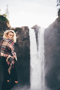 woman holding brown, red, and blue plaid scarf facing waterfalls