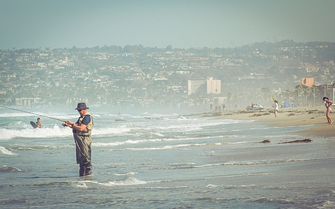 man in brown jumpsuit standing on beach while fishing