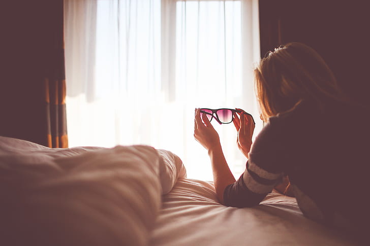 woman holding black sunglasses inside bedroom