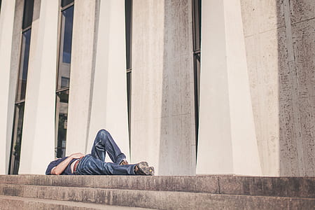 man laying on concrete pavement with stairs near building