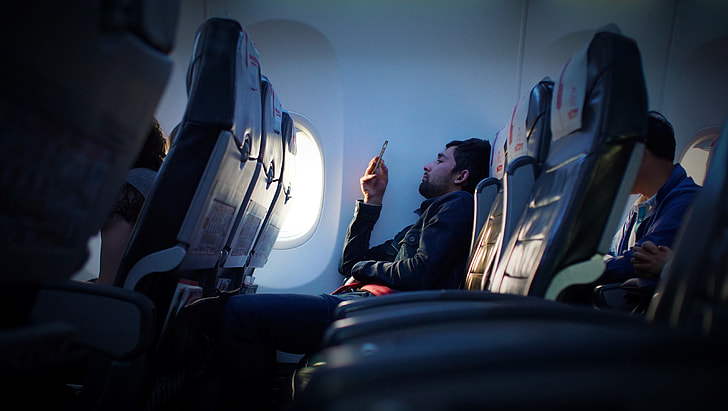 man wearing black dress shirt holding phone in the airplane seat