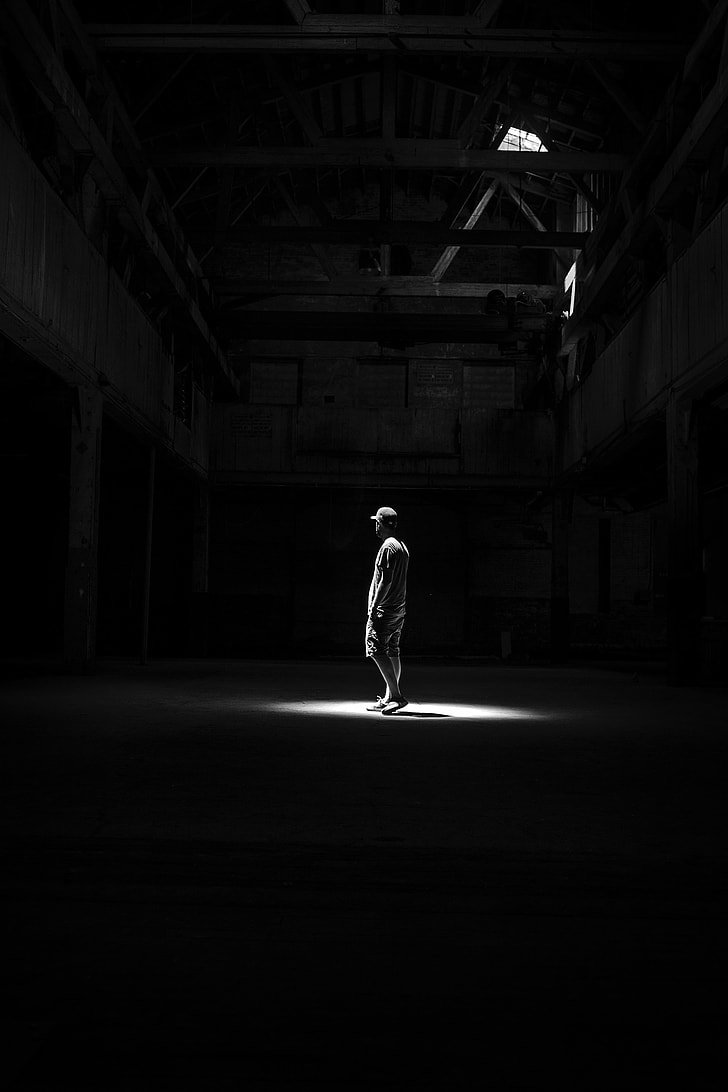 grayscale photography of man standing in room with dim light