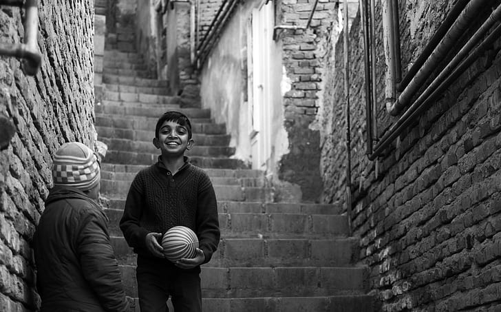 grayscale photography of boy holding ball on stairs