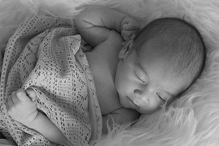 grayscale photography of a baby sleeping on white fur comforter