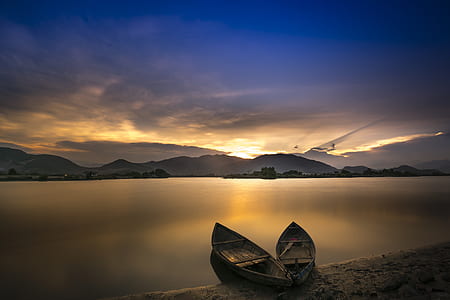 two boats on seashore across mountain during golden hour