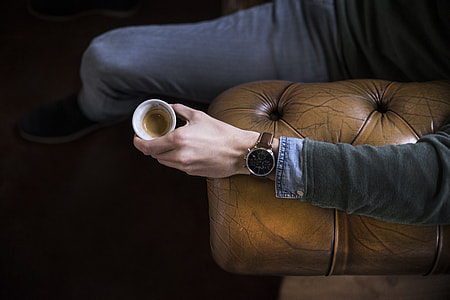 person sitting on brown leather couch holding coffee cup