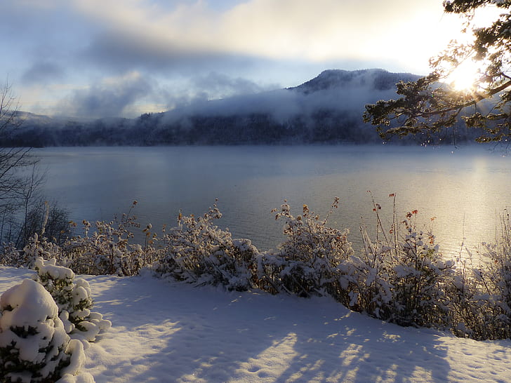 snow covered ground and trees by the river overlooking mountain and sunrise under blue and white cloudy sky