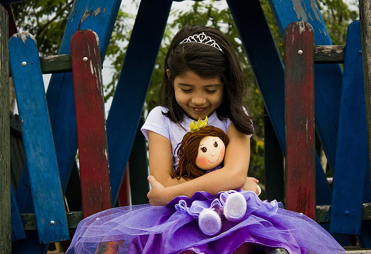 girl in purple t-shirt dress holding rag doll during daytime