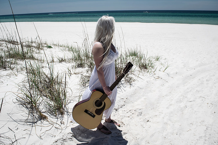 woman wearing white dress holding beige acoustic guitar on sea shore