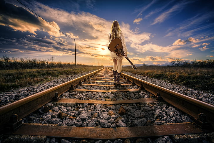 woman carrying acoustic guitar standing on railroad during daytime