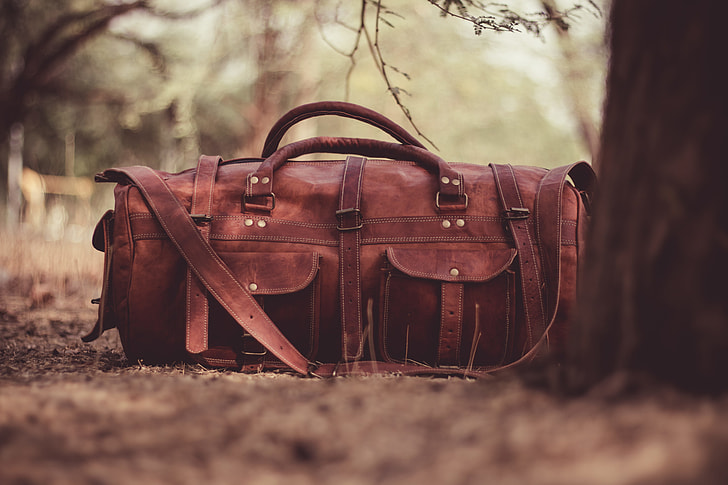 brown leather satchel duffel bag beside brown tree during daytime