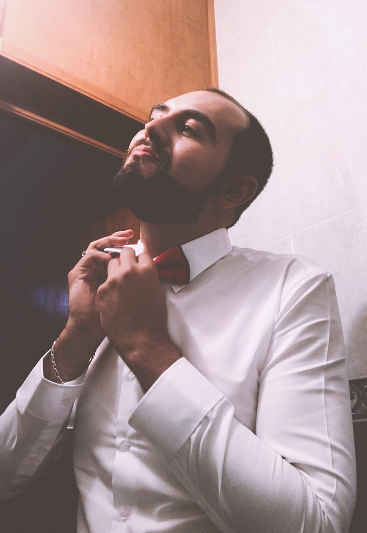 Man in White Dress Shirt Tying a Red Bow Tie
