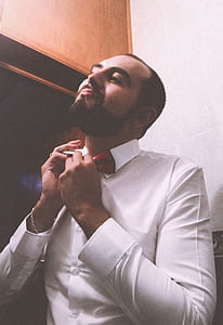 Man in White Dress Shirt Tying a Red Bow Tie
