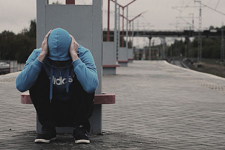 person in blue Adidas zip-up hoodie sitting near post during daytime