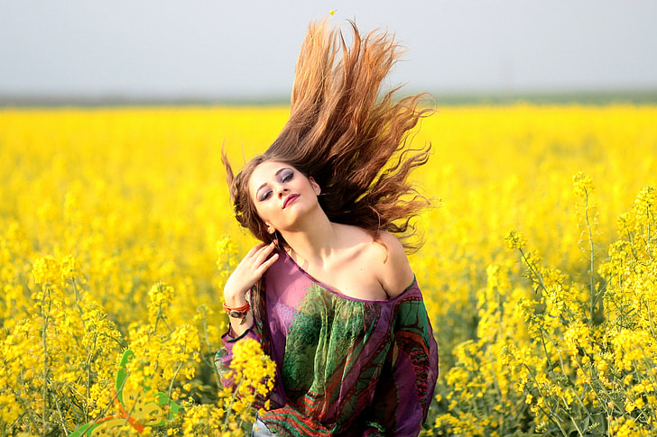 woman wearing purple and green off-shoulder top in yellow rapeseed flower field