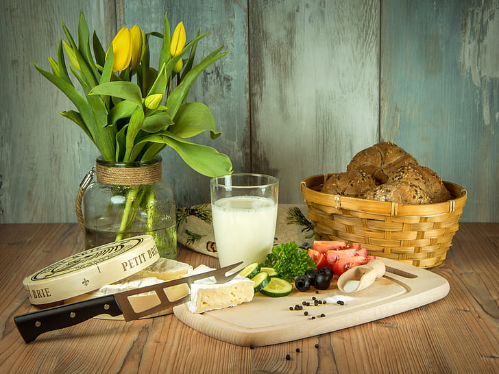 sliced vegetables on chopping board with knife beside glass of milk and basket