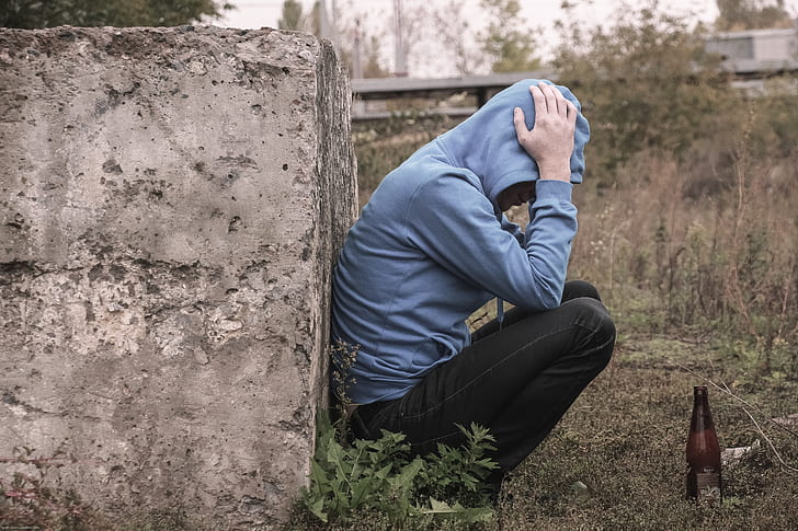 person in blue hoodie leaning on concrete brick