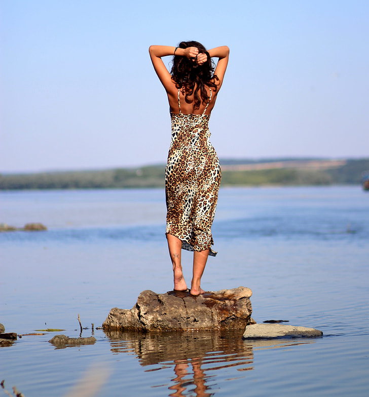 woman standing on brown rock near water during daytime