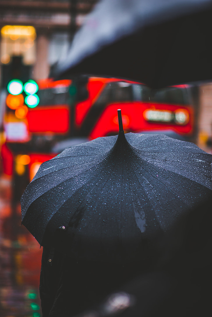 person holding using black umbrella while raining walking outside during daytime