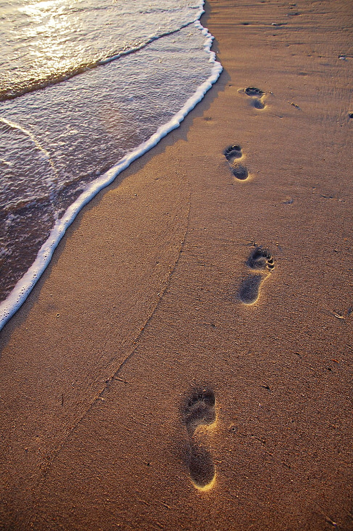 footprints in sand near seawave