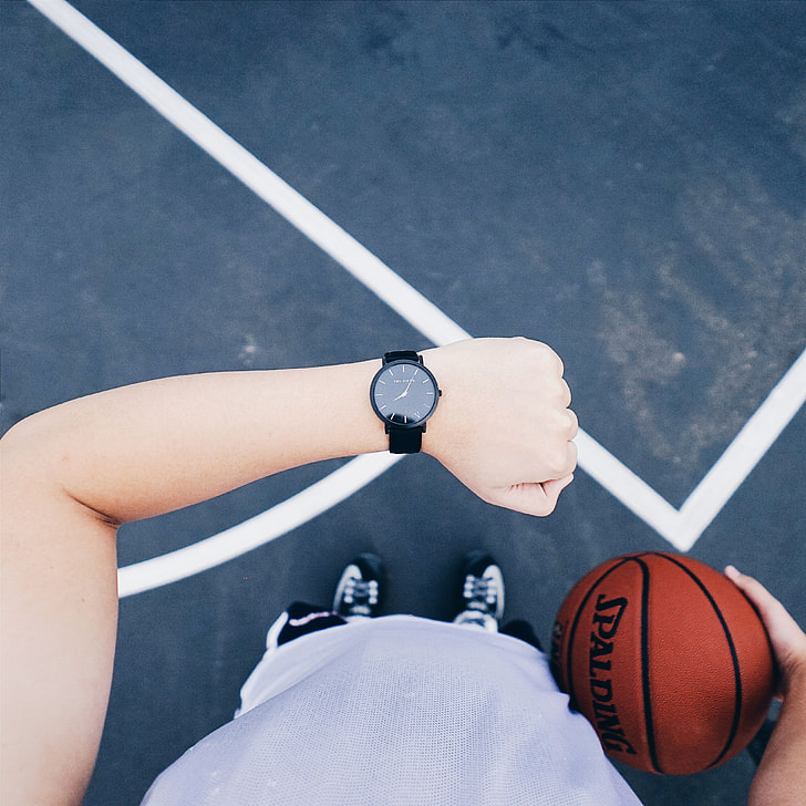 person wearing black analog watch and holding spalding basketball