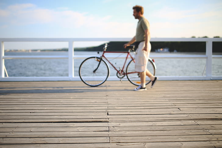 selective focus photography of man holding bicycle on beach deck