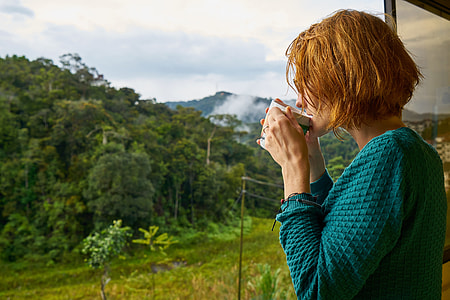 woman in blue long-sleeved top drinking coffee standing in front of mountains