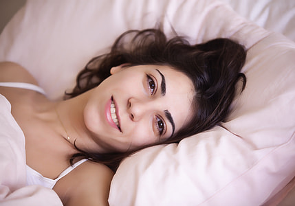 woman lying on bed wearing white spaghetti-strap top