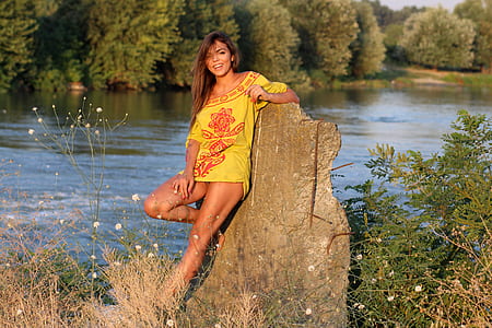 woman in yellow dress lying on rock near body of water during daytime
