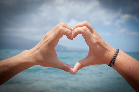 person making heart hand sign in front of sea