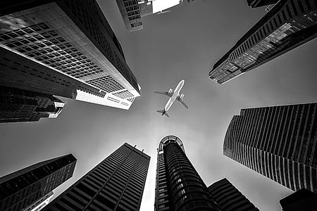low angle and grayscale photo of airplane between tall buildings