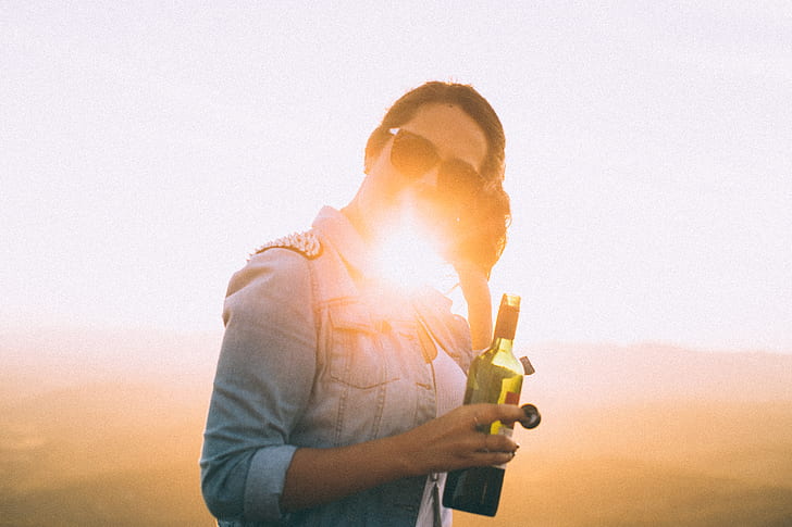 Woman Wearing Blue Denim Jacket Holding Wine Bottle in Golden Hour Photo