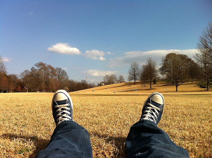 photo of person in black pants and Converse All Star shoes laying on grass