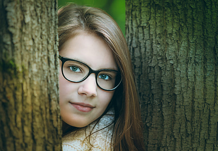 woman wearing black framed eyeglasses between tree during daytime