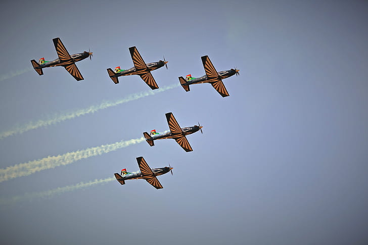 low angle of five black-and-brown planes making smoke trail