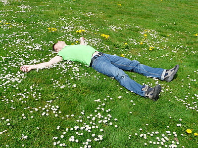 man lying open arms on grass field with flowers